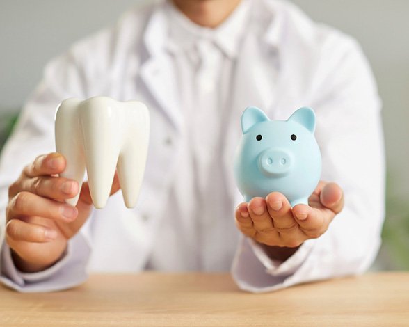 Man holding large model tooth and blue piggy bank