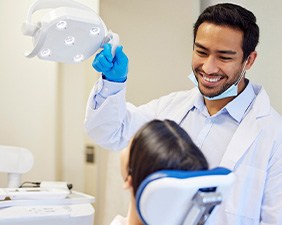 Dentist smiling at patient pulling examination light closer