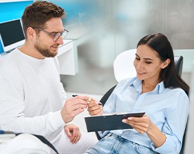 Man in white handing pen to patient to fill out forms on clipboard