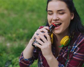 Woman using mouth to open a bottled beverage