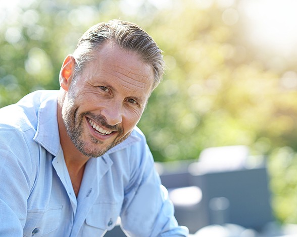 Man in button-up shirt sitting outside and smiling