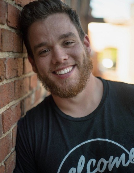 Young smiling man with beard leaning against brick wall
