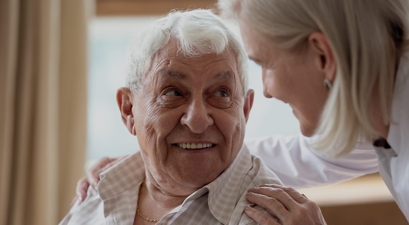 Senior man in chair looking up at standing woman