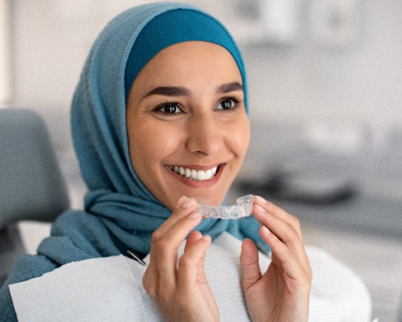 Woman at dental office smiling while holding Invisalign aligner
