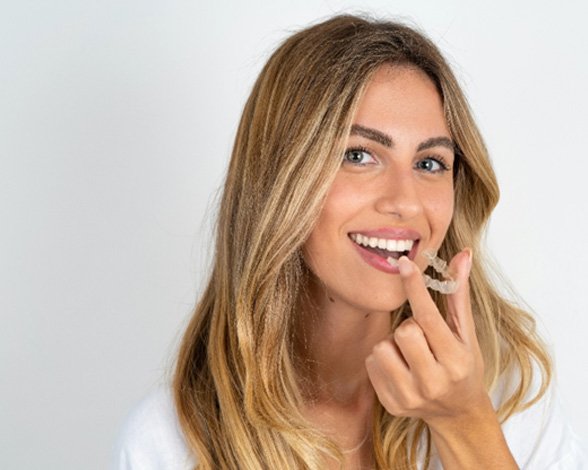 Smiling woman holding Invisalign clear aligner