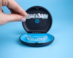 A hand holding an Invisalign aligner over an Invisalign case