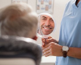 Man smiling while looking at reflection in handheld mirror