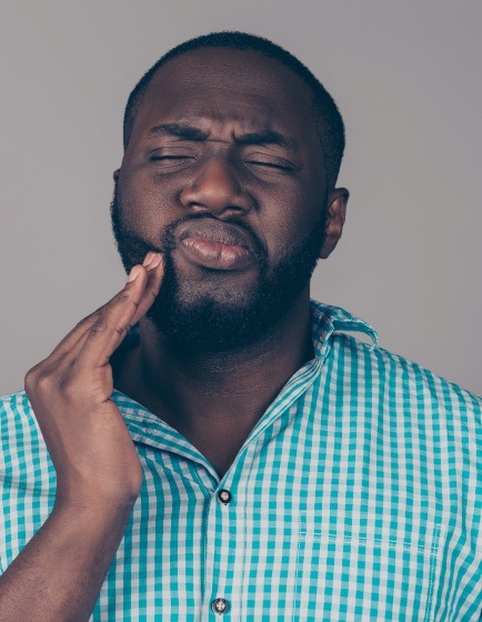 Man in need of emergency dentistry holding cheek in pain