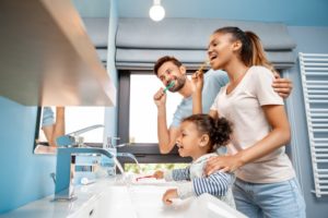 mother, father, and daughter brushing teeth together 